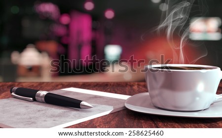 Cafe or bar scene with coffee, notepad and pen on foreground and blurred lights in the background
