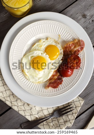 Breakfast with fried eggs, bacon, grilled tomato and orange juice.
