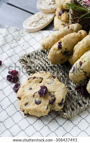 Oatmeal cranberry cookies on a wooden surface with dried cranberries in a basket.