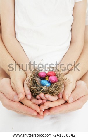 Family Easter - family hands holding brightly colored Easter eggs in a nest