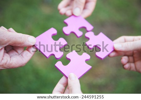 Four hands holding pieces of a pink jigsaw puzzle