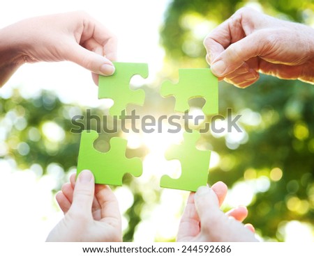 Hands holding up a green jigsaw puzzle against the sunlight
