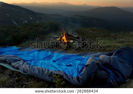 Camp fire beside lake and mountains.