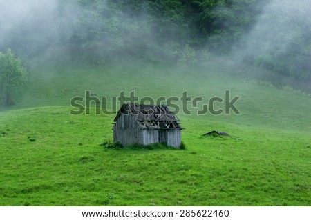 Small old wooden house in foggy forest. Mountains scenery. Nature conceptual image.