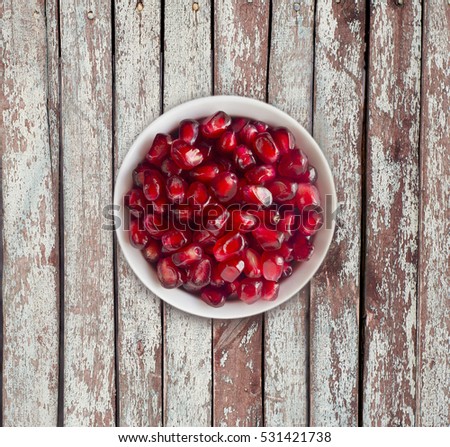 Pomegranate seeds on a wooden background. Red grains of a pomegranate in ceramic bowl. Top view.
