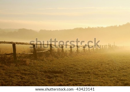 Misty landscape at sunrise with a fence on the pasture of horses. Photo taken in October.