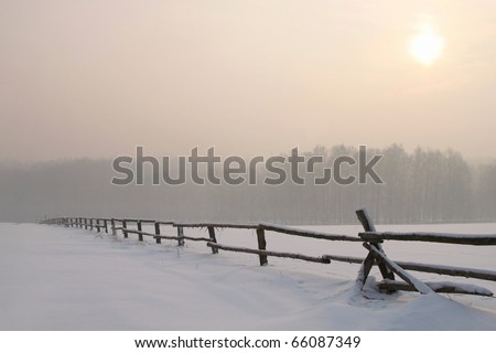 Picturesque sunrise over the field with idyllic fence in the foreground.
