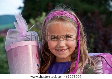 Little school girl with her pink schoolbag and a large cornet of cardboard filled with sweets and little presents given to children  on their first day at school.