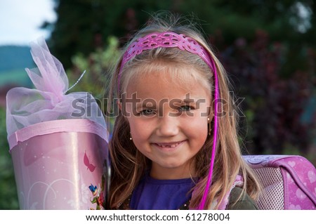 Little school girl with her pink schoolbag and a large cornet of cardboard filled with sweets and little presents given to children  on their first day at school.
