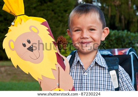 Little school boy with his blue schoolbag and a large cornet of cardboard filled with sweets and little presents given to children on their first day at school.