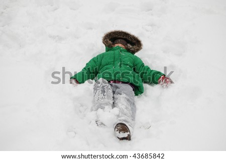 Young child with green jacket laying on a fresh snow outside playing and having fun