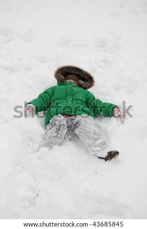 Young child with green jacket laying on a fresh snow outside playing and having fun