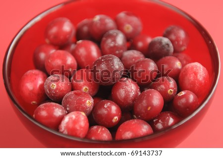 Fresh frozen raw cranberries in a transparent red bowl on a red background