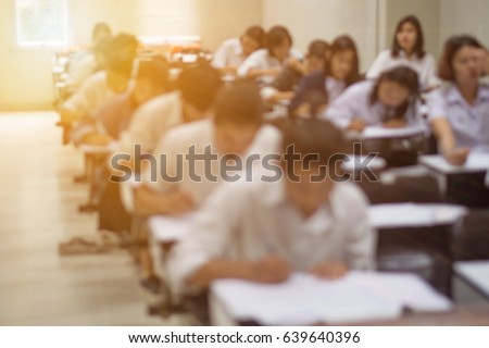 Blur abstract background of examination room with undergraduate students inside. Blurred view of student doing final test in exam hall. Blurry view of study chairs in classroom of university or campus