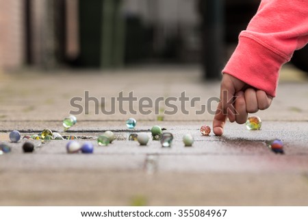 Child playing with marbles on yhe sidewalk.\
old-fashioned toys still in use today.