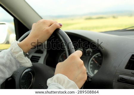 Young woman driving car - hands of a driver on steering wheel of a car
