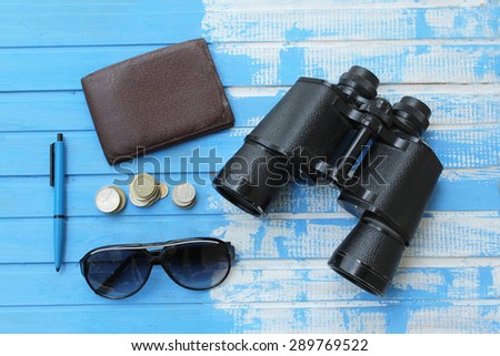 Preparation for travel - wallet, binoculars, sunglasses, money, pen - on blue wooden table