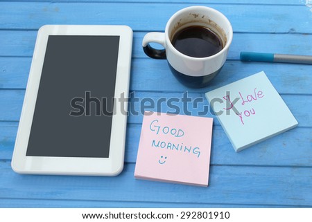 Touch screen tablet computer, cup of coffee, sticky note with good morning and I love you message - on blue background