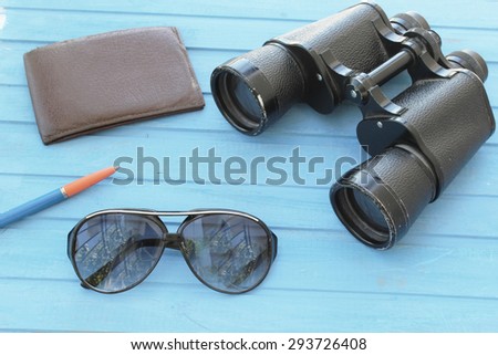 Preparation for travel - wallet, binoculars, sunglasses and pen - on blue wooden table