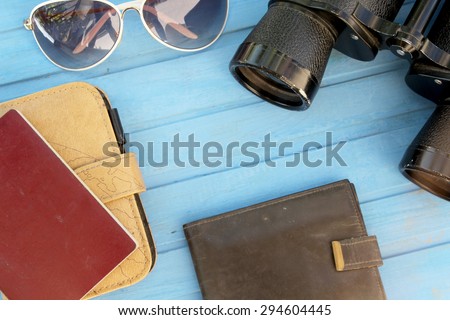 Preparation for travel - binoculars, passport, wallet, notebook and sunglasses - on blue wooden table - vintage style