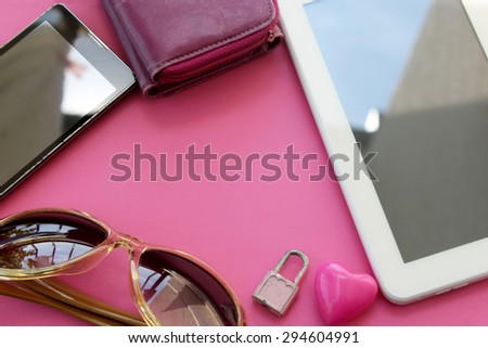 Set of woman\'s everyday objects - smartphone, wallet, tablet computer, sunglasses, padlock and heart on pink background - copy space