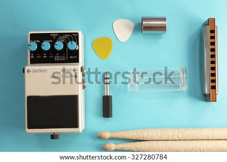 Music concept - guitar pedal, drum sticks, harmonica, audio plug, guitar slide and guitar picks on blue background