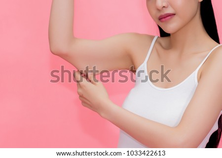 Young attractive Asian woman pinching excess fat and cellulite in her upper arms as she lacks exercise and healthy lifestyle
