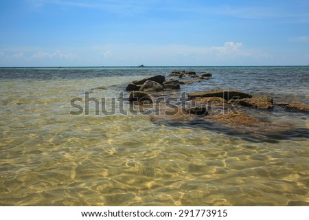 Rocks path on the beach, rocks and beach during sunny day on blue sky and sea