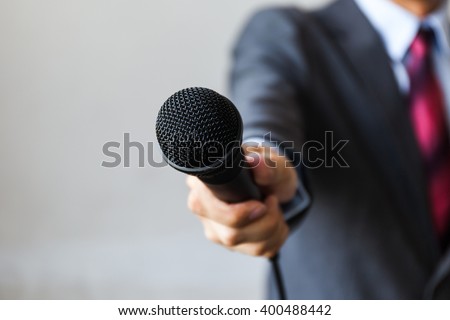Man in business suit holding a microphone conducting a business interview, journalist reporting, public speaking, press conference, MC