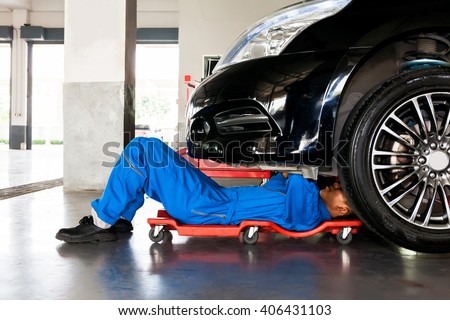 Mechanic in blue uniform lying down and working under car at auto service garage