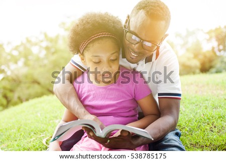 African American family reading a book together in the outdoor park