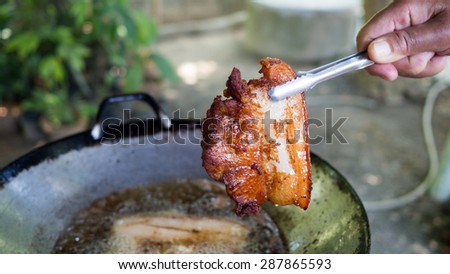 Local traditional Thai kitchen. Hand holding Serving kitchen tongs fried pork from the traditional pan.