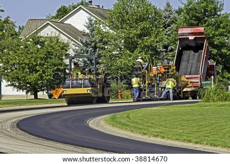 Steamroller and dump truck crews laying new pavement in a residential neighborhood