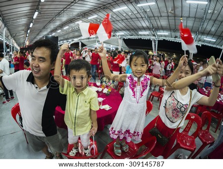 SINGAPORE - AUGUST 8 : A young family sing one of the national day song and wave mini national flags with pride and joy at Pasir Ris - Punggol SG50 National Day dinner event on Aug 8, 2015, Singapore