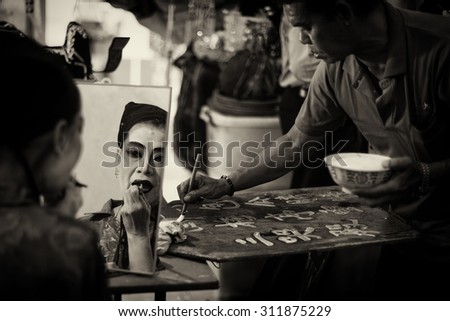 SINGAPORE - AUG 20: Dark sepia version of Chinese Teochew opera singer makeup and man writing the programme for the day on Aug 20, 2015 in SINGAPORE.