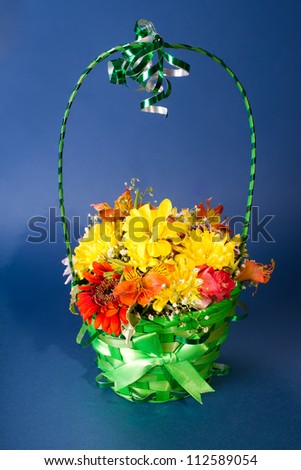 Colorful flowers fill green basket on blue background