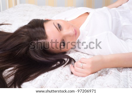 Portrait of brunette woman on the bed with white bed linen.