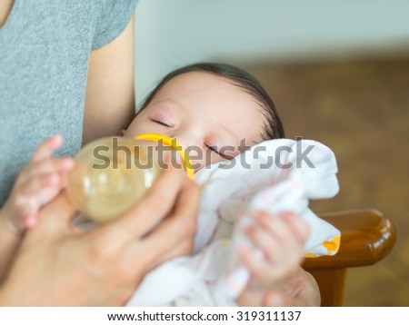 Asian mother feeding bottle her baby while baby sleeping.