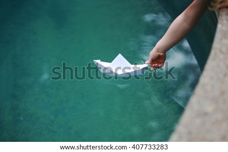 A kid putting a paper boat into water