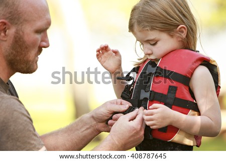 A father helping his daughter with her life jacket