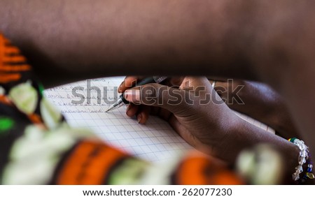 African Education Symbol: Writing A Letter. A young African girl writes down a letter to a friend of hers with a black pen.