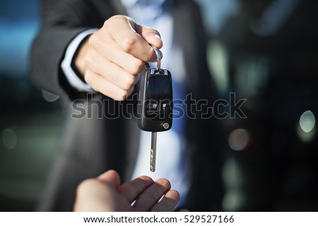 male adult dealer hand giving car keys to female person, close-up photo outdoor, sunny day, caucasian man in suit