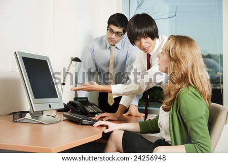 Business colleagues gathered around a computer screen, one of them explaining the contents of the computer screen.
