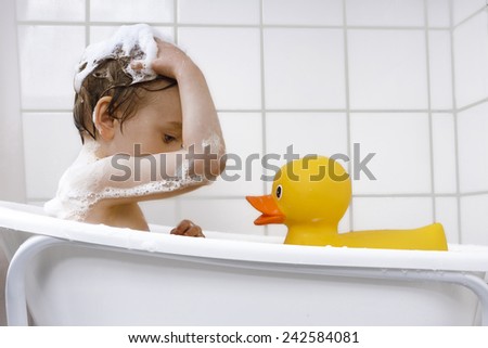 Cute boy washing hair in bathtub with rubber duck
