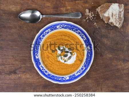 top view of a pumpkin soup with a spoon and chunk of bread on wooden cutting board