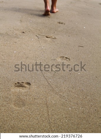 woman walking on sand beach leaving footprints in the sand