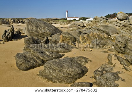 Coastline stones in the east of Yeu island surrounded with sand, the lighthouse of Pointe des Corbeaux is at background