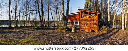 Traditional Finish Sauna colored in red is in the border of lake in the forest. This typical wooden construction in Finland has a dry firewood storage place, Rajamaki, Saaksjarvi lake in spring