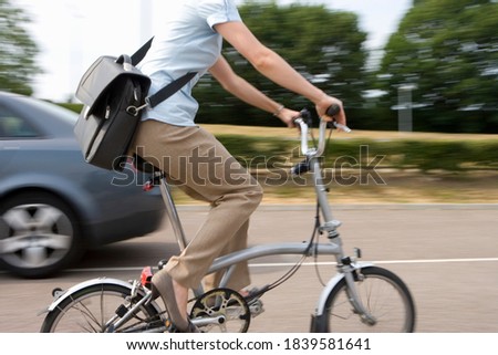 Motion blur of mid-section of a young woman with a sling bag on a bicycle riding on a street.
