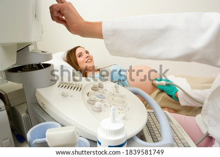 Portrait of a pregnant woman undergoing an ultrasound scan looks up at the doctor pointing at the monitor.